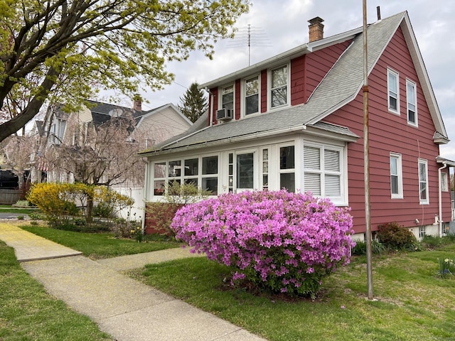 view of front of home featuring cooling unit, a chimney, a front yard, and a shingled roof