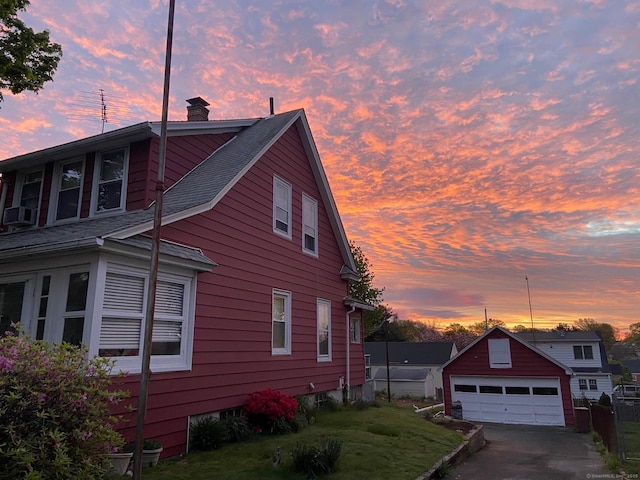 property exterior at dusk with fence, roof with shingles, a chimney, a garage, and an outdoor structure