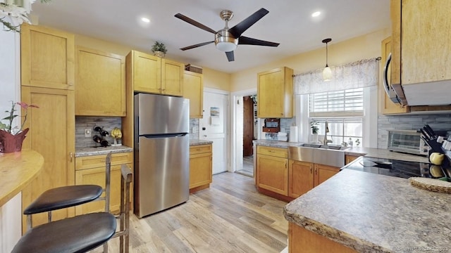 kitchen with decorative backsplash, freestanding refrigerator, a sink, and light wood finished floors