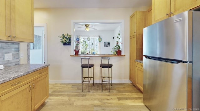 kitchen featuring light wood-type flooring, backsplash, freestanding refrigerator, and baseboards