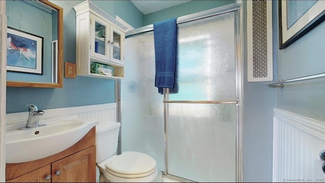 bathroom with a stall shower, a wainscoted wall, vanity, and toilet