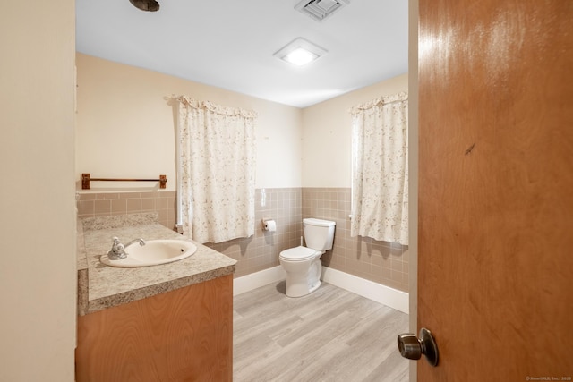 half bath featuring visible vents, toilet, vanity, wood finished floors, and tile walls