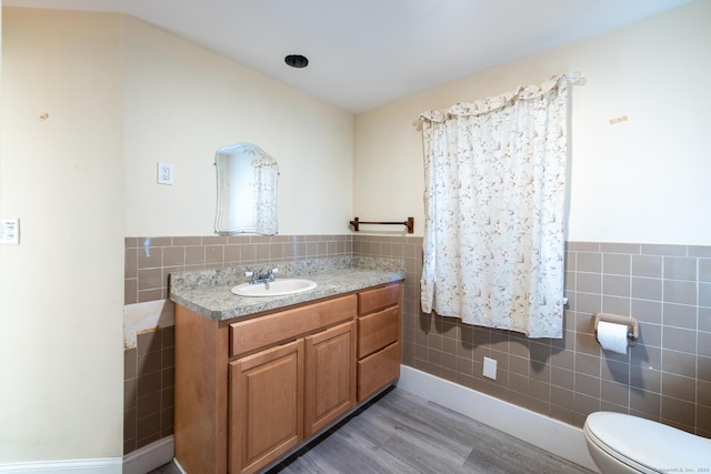 bathroom featuring a wainscoted wall, toilet, wood finished floors, tile walls, and vanity