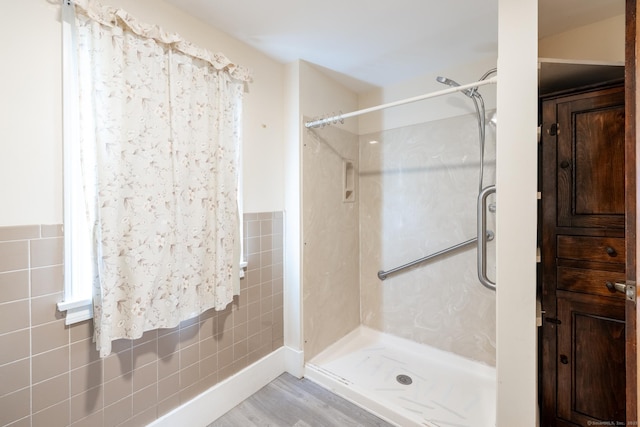 full bathroom featuring a wainscoted wall, wood finished floors, tile walls, and a stall shower