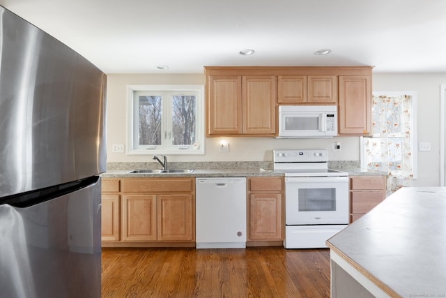 kitchen with light brown cabinetry, a sink, dark wood finished floors, white appliances, and light countertops