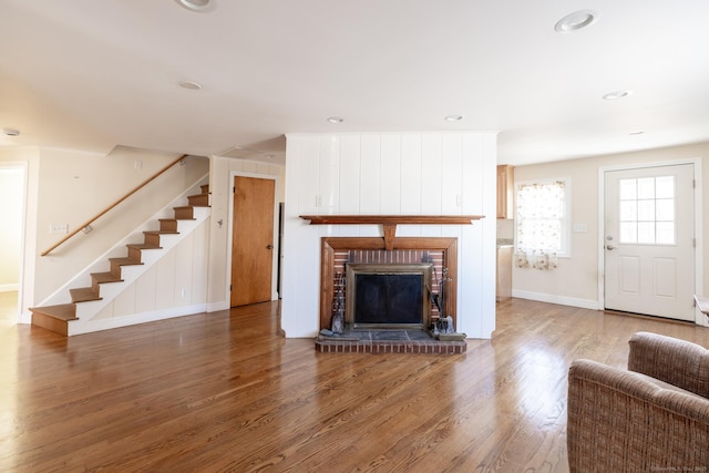 unfurnished living room featuring stairway, wood finished floors, baseboards, recessed lighting, and a brick fireplace