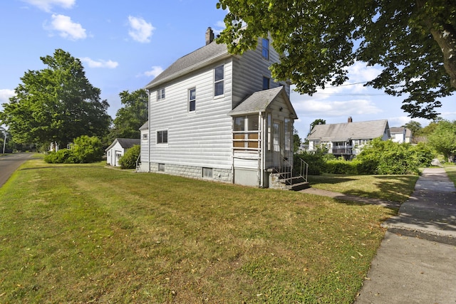 view of side of property with entry steps, a shingled roof, a chimney, and a lawn