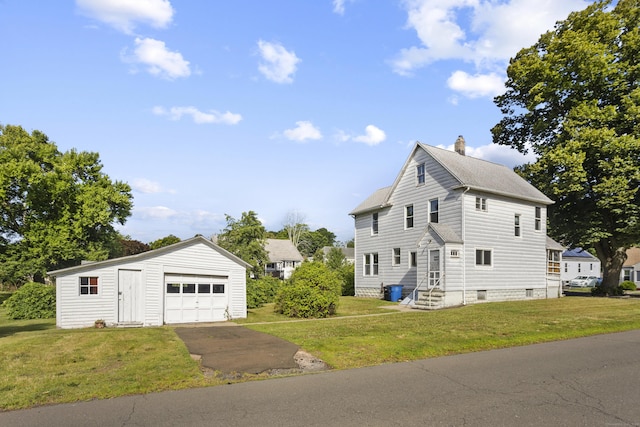 view of front of property featuring a garage, driveway, a front lawn, and an outbuilding