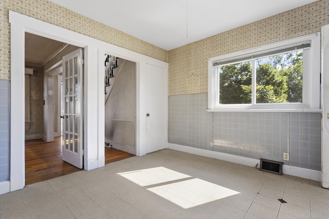 empty room with a wainscoted wall, tile patterned flooring, tile walls, and wallpapered walls