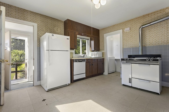 kitchen with light countertops, dark brown cabinetry, a sink, white appliances, and wallpapered walls