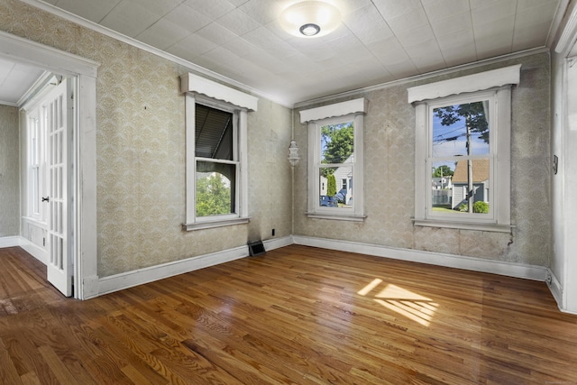 empty room with wood finished floors, crown molding, baseboards, and wallpapered walls