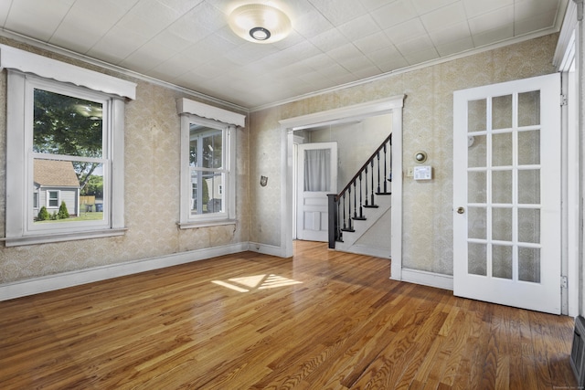 spare room with baseboards, ornamental molding, wood finished floors, and wallpapered walls