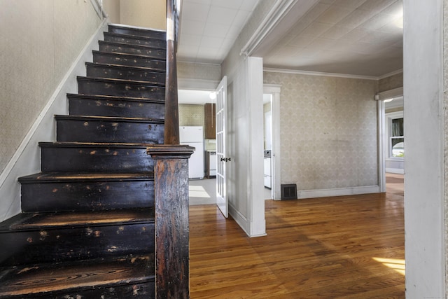 stairs with wallpapered walls, baseboards, visible vents, ornamental molding, and wood finished floors