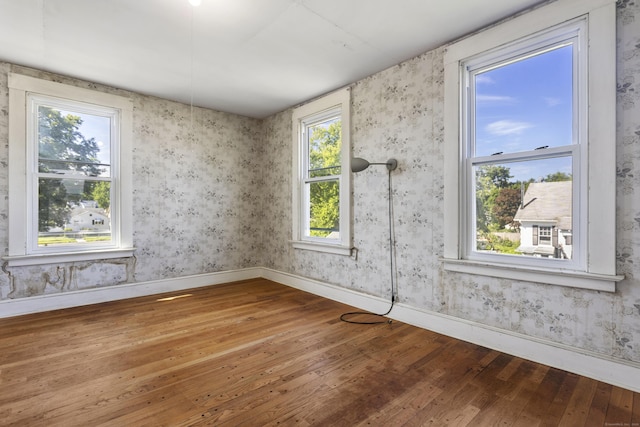 unfurnished room featuring wallpapered walls, wood-type flooring, and baseboards