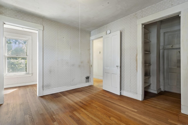 unfurnished bedroom with baseboards, a spacious closet, hardwood / wood-style floors, and wallpapered walls