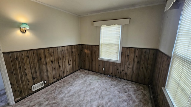 unfurnished room with wooden walls, visible vents, a wainscoted wall, ornamental molding, and carpet floors