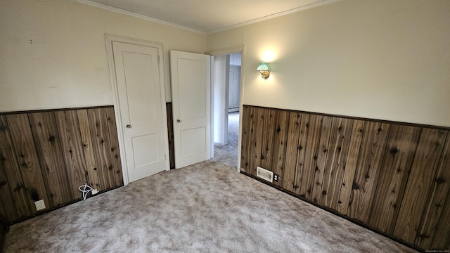 spare room featuring a wainscoted wall, carpet, wood walls, and crown molding