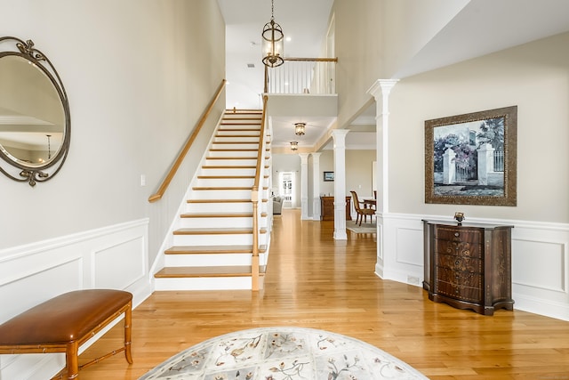 foyer entrance featuring stairs, a decorative wall, light wood-style floors, and ornate columns