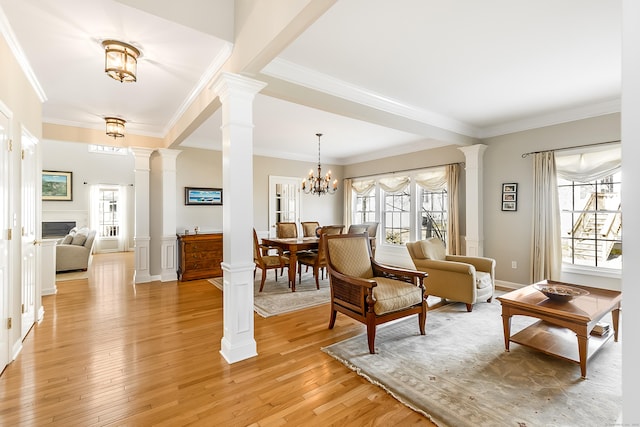 sitting room featuring light wood finished floors, crown molding, ornate columns, a fireplace, and a notable chandelier