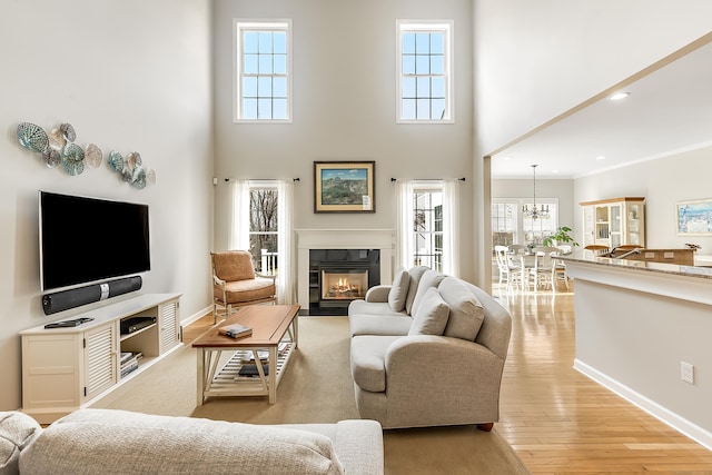 living room with recessed lighting, a high ceiling, a fireplace with flush hearth, light wood-type flooring, and baseboards