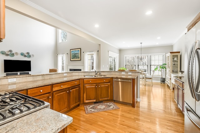 kitchen featuring brown cabinets, crown molding, appliances with stainless steel finishes, a sink, and light wood-type flooring