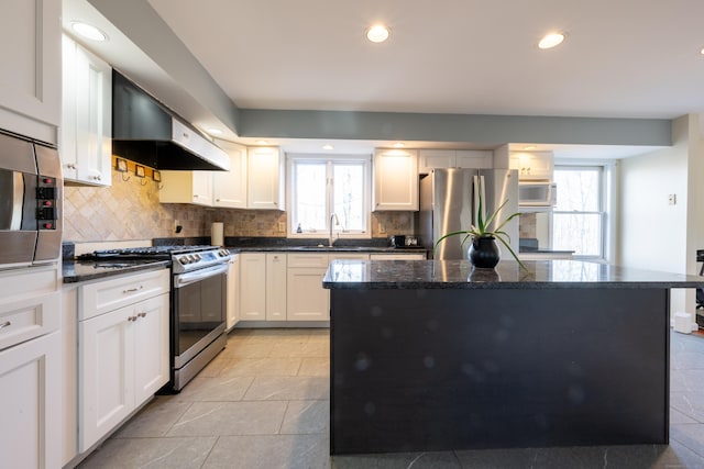 kitchen with a kitchen island, plenty of natural light, stainless steel appliances, and wall chimney range hood