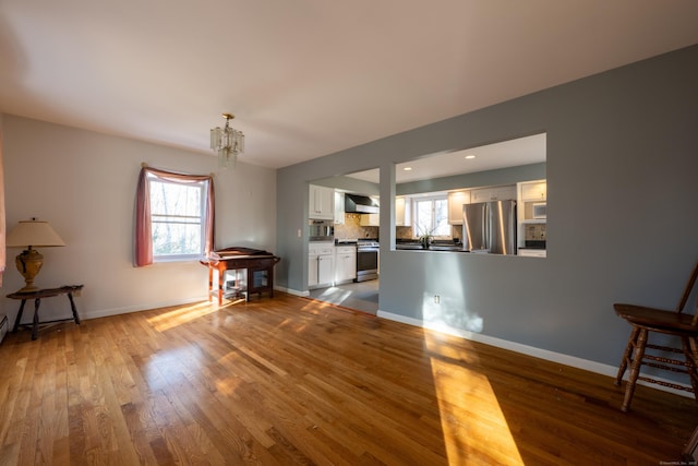 unfurnished living room featuring recessed lighting, baseboards, an inviting chandelier, and wood finished floors