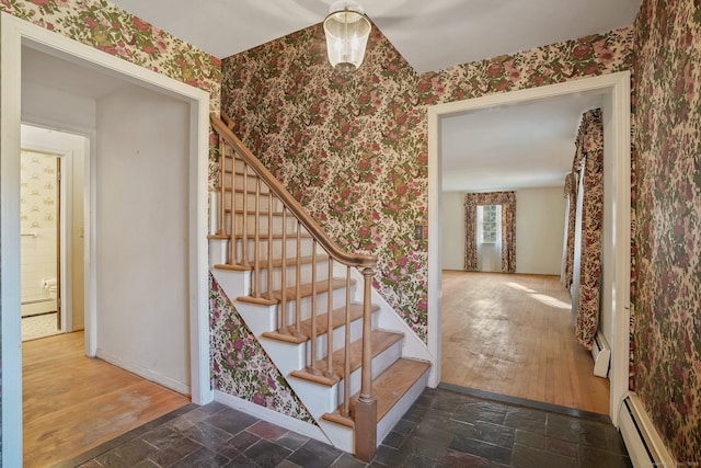 stairway with a baseboard radiator, baseboards, stone tile flooring, and wallpapered walls