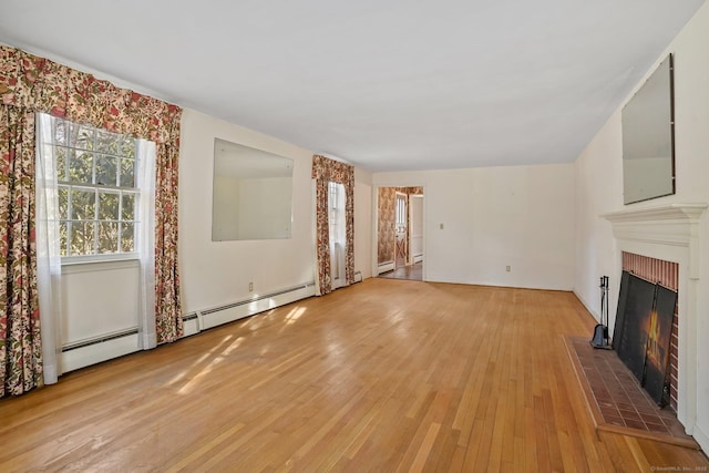 unfurnished living room featuring a baseboard heating unit, a warm lit fireplace, and light wood finished floors