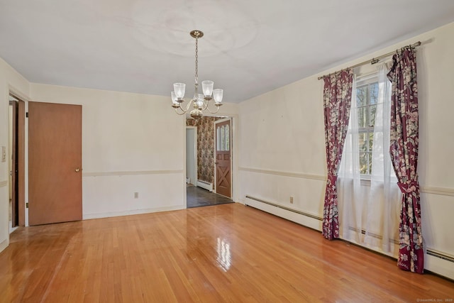 spare room featuring a baseboard heating unit, wood finished floors, baseboards, and a chandelier