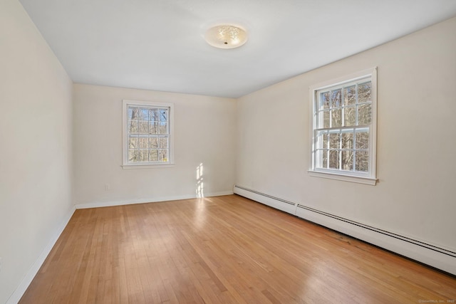 spare room featuring light wood finished floors, a baseboard heating unit, and baseboards