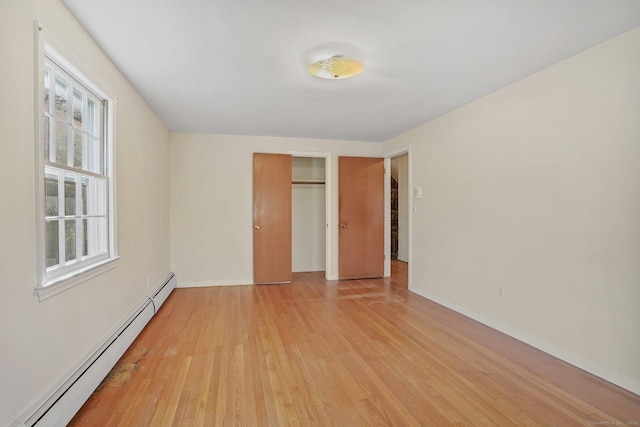 unfurnished bedroom with a baseboard radiator, multiple windows, and light wood finished floors