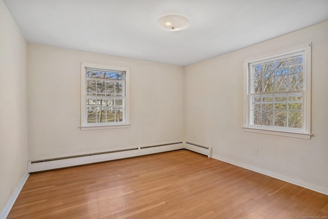 empty room featuring a wealth of natural light, light wood finished floors, baseboards, and baseboard heating