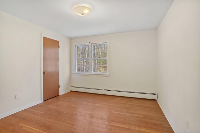 empty room featuring a baseboard heating unit, baseboards, and light wood-style flooring