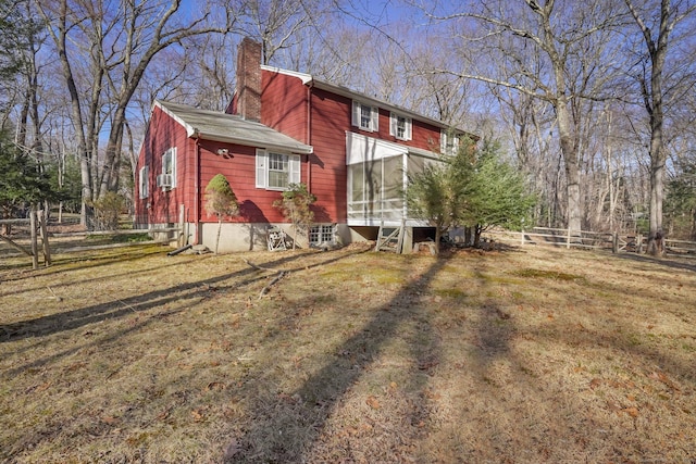 view of home's exterior featuring fence, a lawn, a sunroom, and a chimney