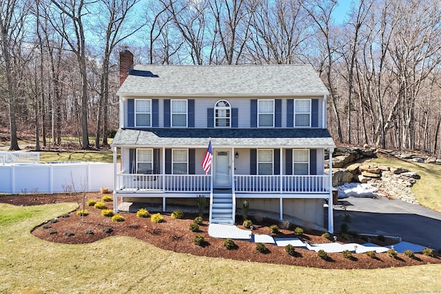 view of front of home featuring a chimney, aphalt driveway, covered porch, fence, and a front lawn