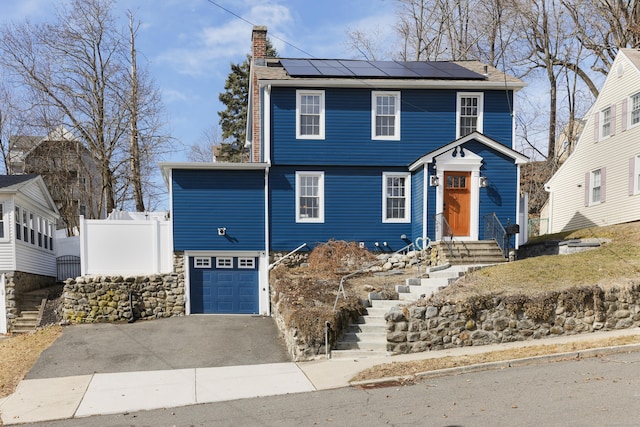 colonial house with solar panels, aphalt driveway, a garage, and a chimney