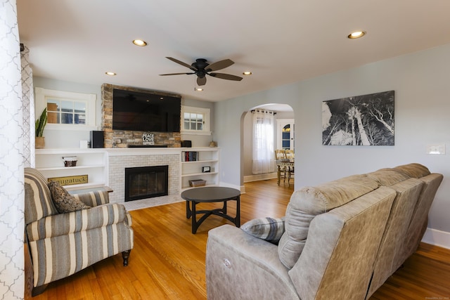 living room featuring wood finished floors, recessed lighting, arched walkways, baseboards, and a brick fireplace