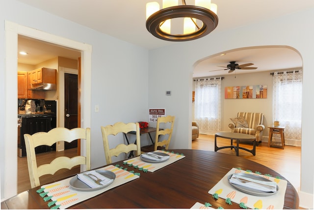 dining area featuring arched walkways, a ceiling fan, and light wood finished floors