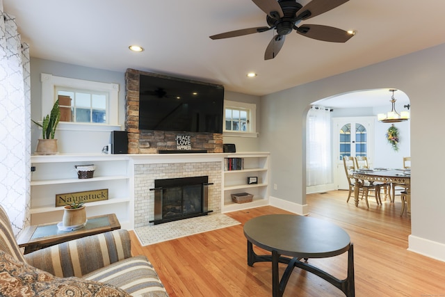 living area featuring baseboards, recessed lighting, a fireplace, wood finished floors, and arched walkways