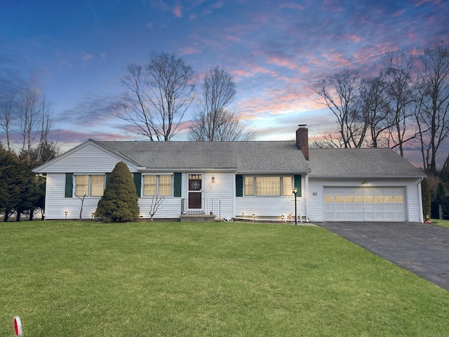 ranch-style home with aphalt driveway, a yard, roof with shingles, an attached garage, and a chimney