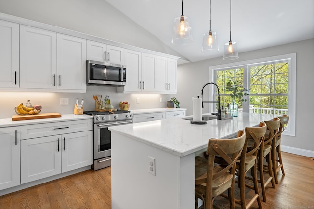 kitchen featuring a kitchen island with sink, a sink, stainless steel appliances, vaulted ceiling, and light wood-type flooring