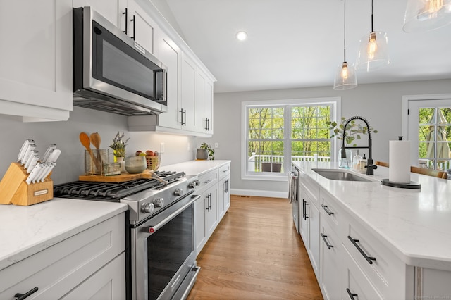 kitchen with pendant lighting, light wood-type flooring, appliances with stainless steel finishes, white cabinetry, and a sink