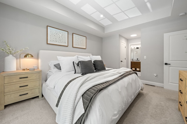 bedroom featuring a tray ceiling, light carpet, baseboards, and ensuite bathroom