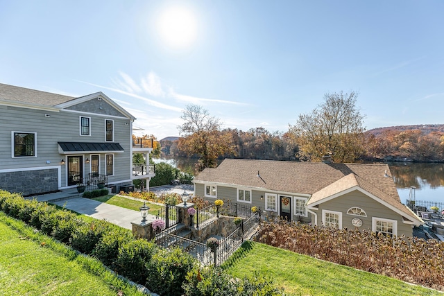 view of front facade with a shingled roof, a front yard, fence, and a water view