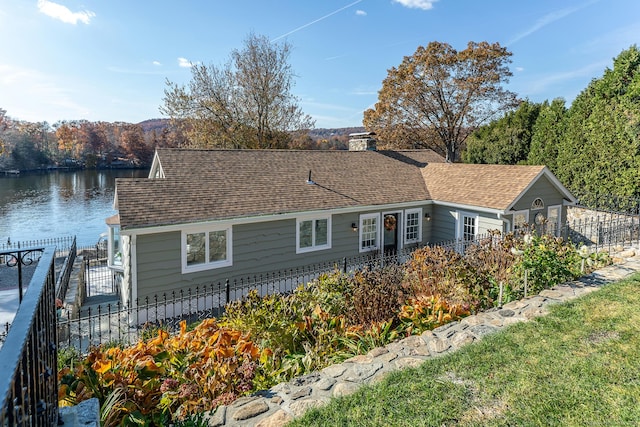 view of front facade with roof with shingles, fence, a chimney, and a water view