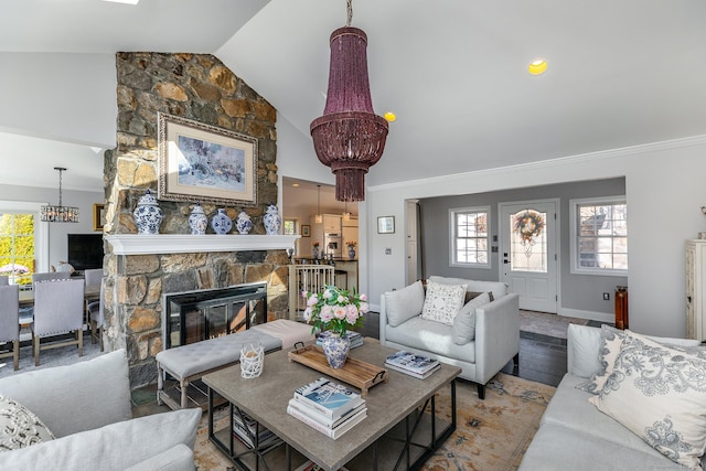 living room featuring lofted ceiling, ornamental molding, wood finished floors, an inviting chandelier, and a stone fireplace