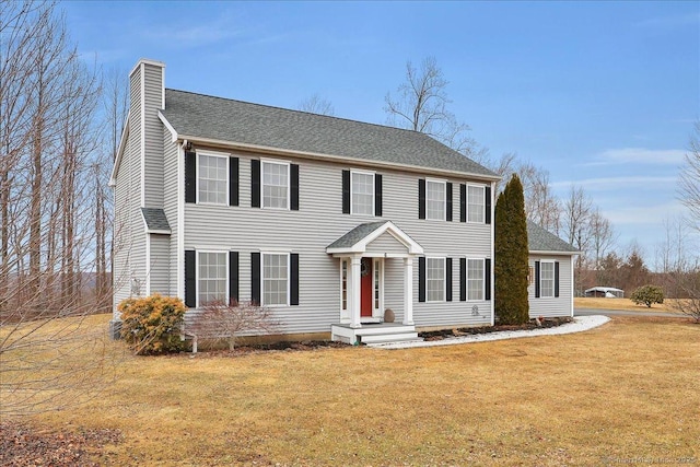 colonial house featuring a front lawn, roof with shingles, and a chimney