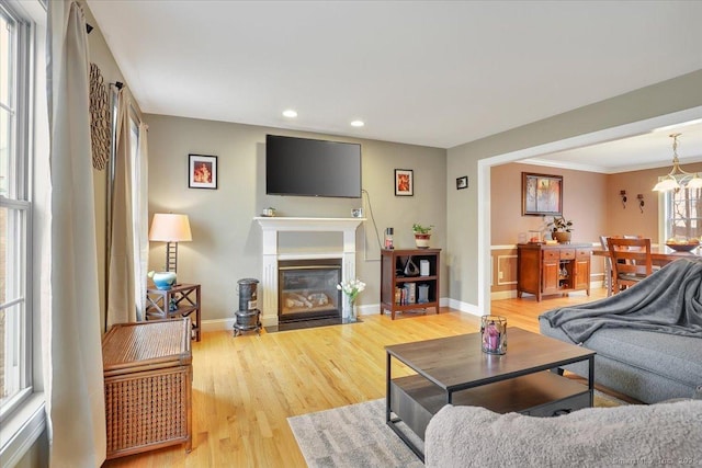 living area with a fireplace with flush hearth, recessed lighting, baseboards, and light wood finished floors