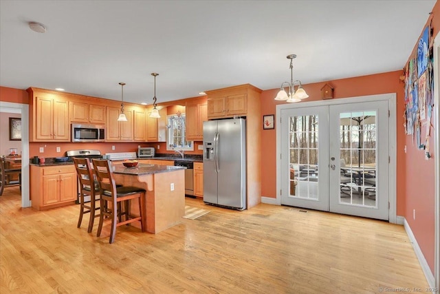 kitchen featuring light brown cabinets, a center island, appliances with stainless steel finishes, french doors, and light wood-style floors